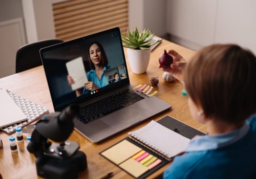 A Preteen boy uses a laptop to make a video call with his teacher. The Screen shows an online lecture with a teacher explaining the subject from class.